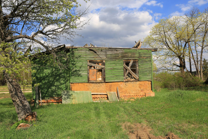Abandoned green wooden house with broken windows surrounded by trees and grass, evoking scary moments and trauma.