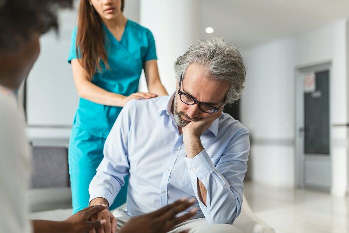 Middle-aged man looking worried during medical consultation with nurse and doctor, reflecting wild patient confessions heard by doctors