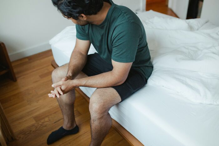 Man sitting on edge of bed in casual clothes, reflecting on wild patient confessions doctors have truly heard