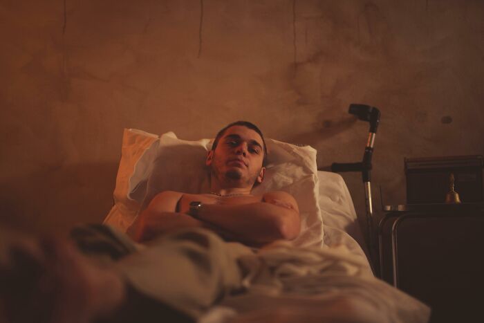 Young male patient lying in bed with a cane nearby, reflecting wild patient confessions doctors have heard.