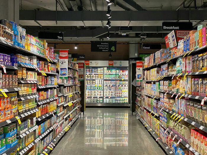 Grocery store aisle filled with breakfast cereals and tea, showing prices and product variety under bright store lights.