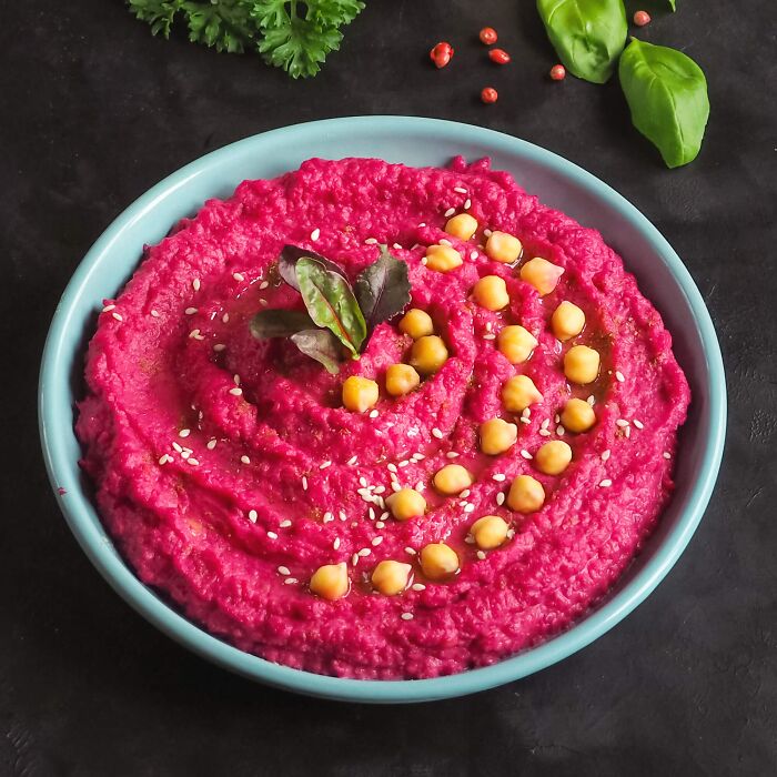 Bright beet hummus topped with chickpeas and greens in a bowl, showcasing dishes foodies say don't need a gourmet upgrade.