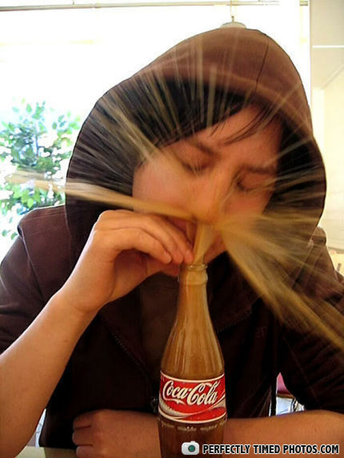 Person in hoodie having soda spray burst from bottle, captured in a perfectly timed photo with dynamic motion effect.