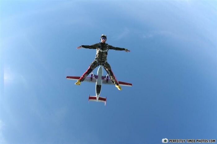 Skydiver in midair perfectly timed photo with airplane flying beneath against a clear blue sky background