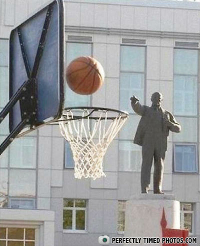 Basketball captured mid-air just before going through the hoop in a perfectly timed photo with a statue in the background.