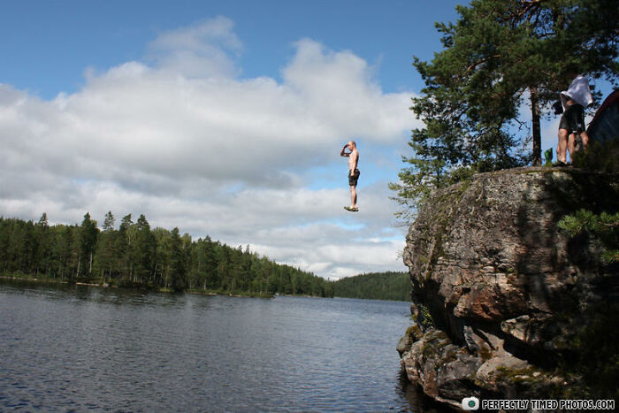 Person captured mid-air while cliff jumping into a lake, showcasing one of the perfectly timed photos.