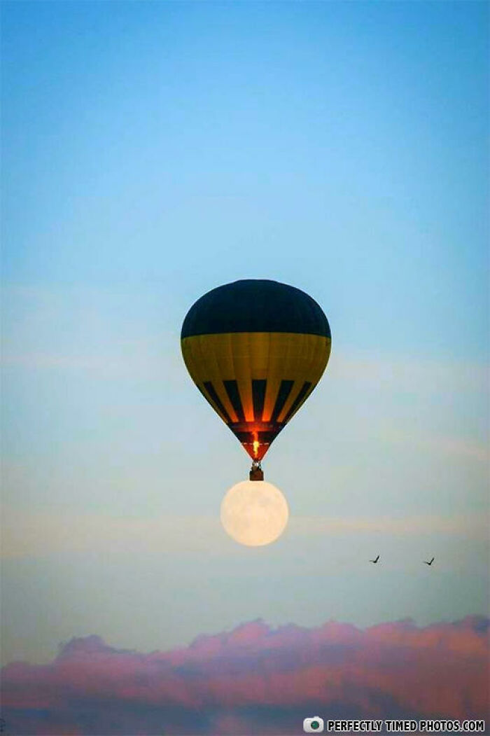 Hot air balloon perfectly timed to appear as if holding the rising full moon above colorful clouds in an impressive photo.