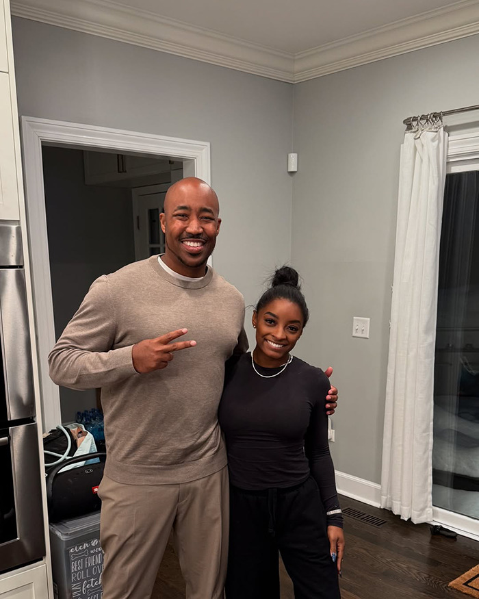 Simone Biles smiling indoors with a man, posing casually amid a home setting, related to painful dog ears controversy.