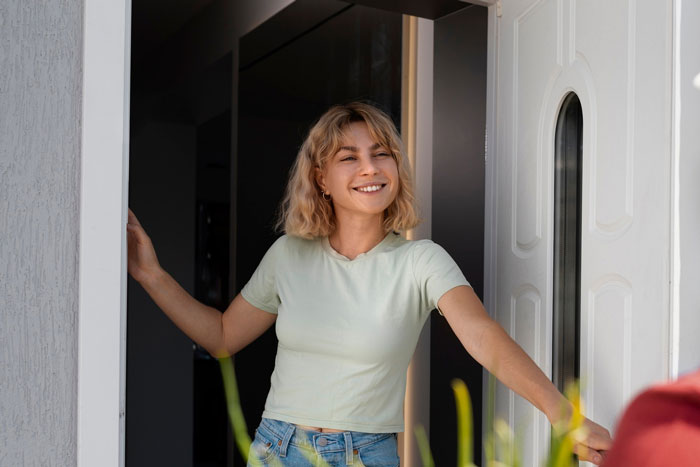 Young woman smiling at the doorway with sunlight, representing a friendly Karen Petty fence revenge moment outdoors.