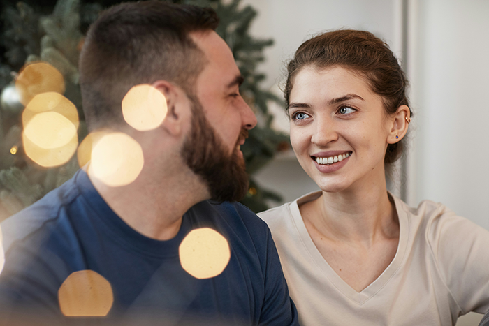 Couple smiling and talking near Christmas tree, reflecting a holiday moment tied to PS5 gift expectations and surprise.