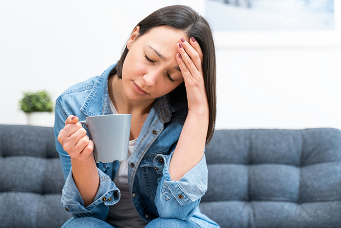 Woman sitting on couch with coffee, looking stressed after guy pressures girlfriend about PS5 for Xmas gift.