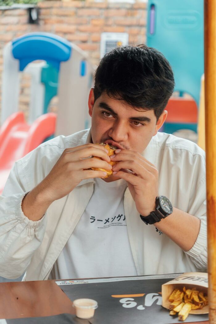 Young man eating a burger with fries nearby, capturing funny and clever moments in the heat of the moment.