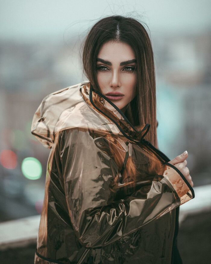 Woman wearing a transparent shiny raincoat posing outdoors, showcasing unusual personal belongings fashion style.