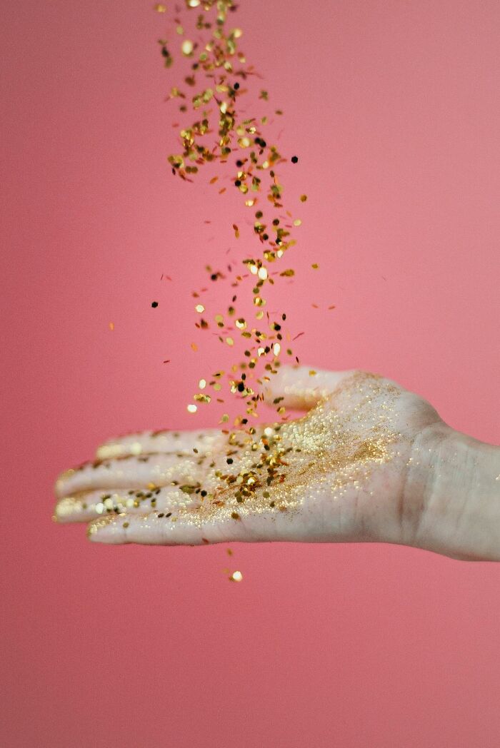 Hand catching falling golden glitter on pink background, symbolizing brilliantly sneaky acts of revenge creativity.