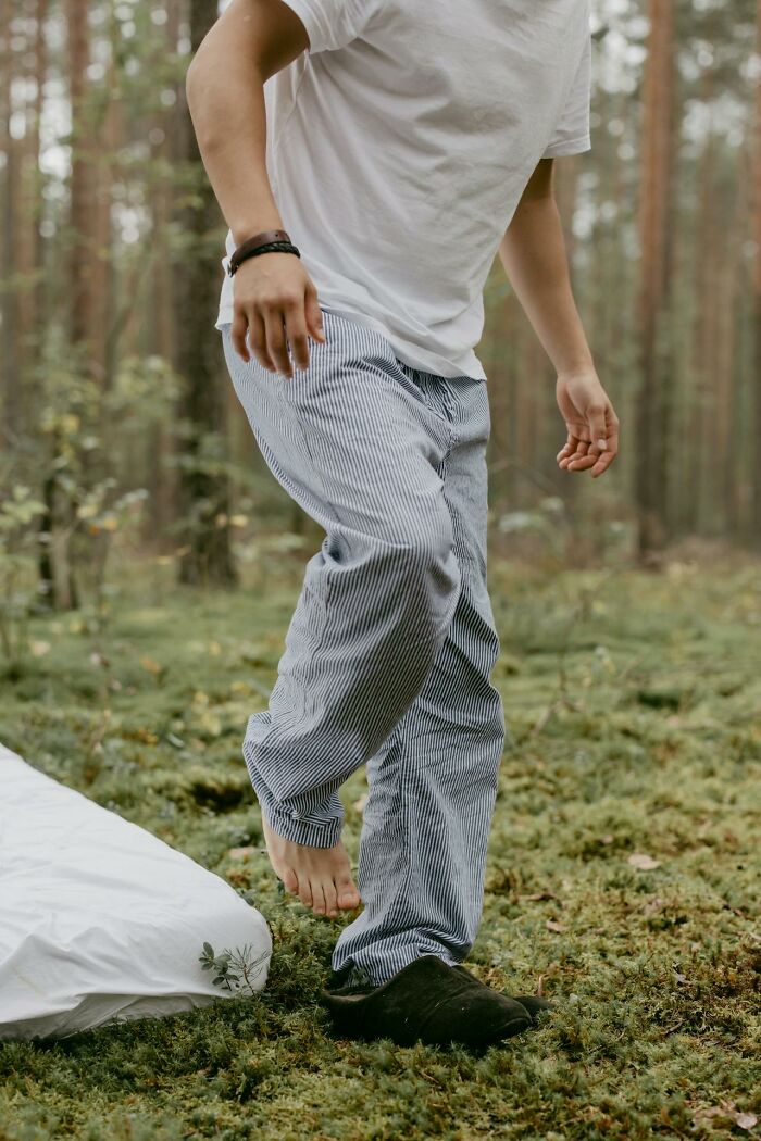 Person in striped pants and white shirt walking barefoot on mossy ground in a forest setting for airport stories concept