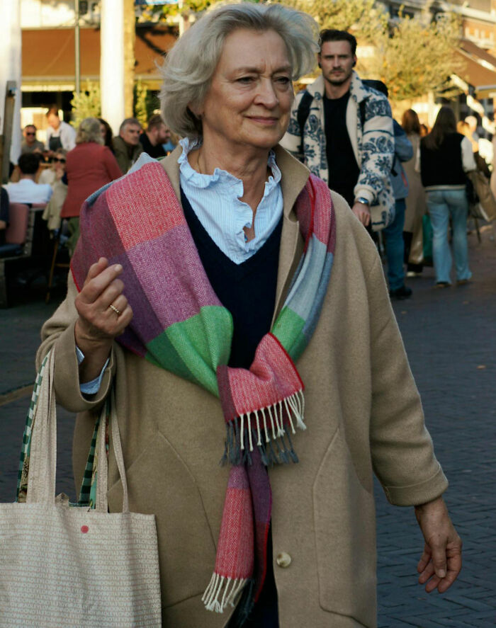 Elderly woman walking outdoors wearing a colorful scarf and carrying a tote bag with airport stories theme.