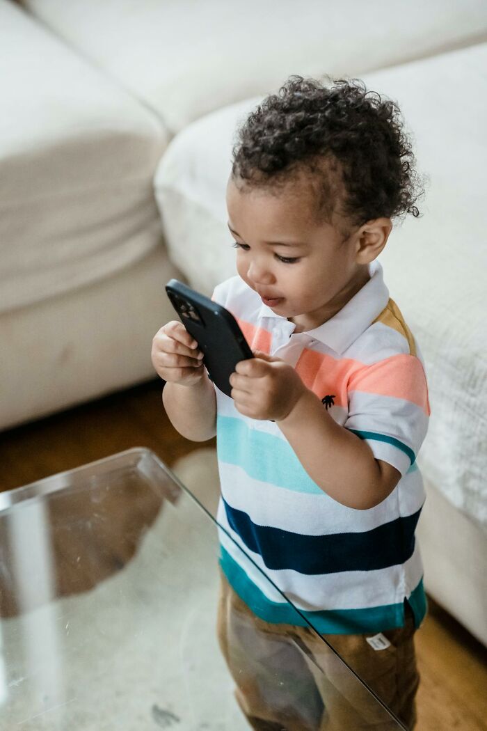 Toddler holding a smartphone indoors, illustrating modern parenting trends and the impact of technology on children.