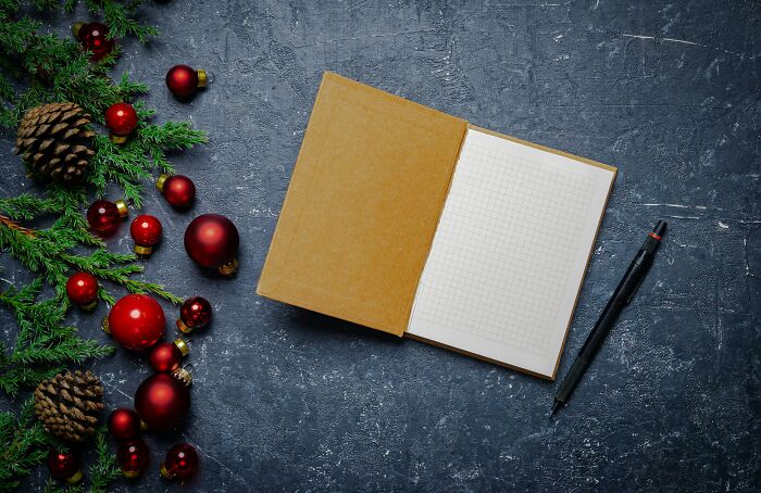 Empty notebook with pen beside Christmas decorations and pinecones representing horrible gifts concept.