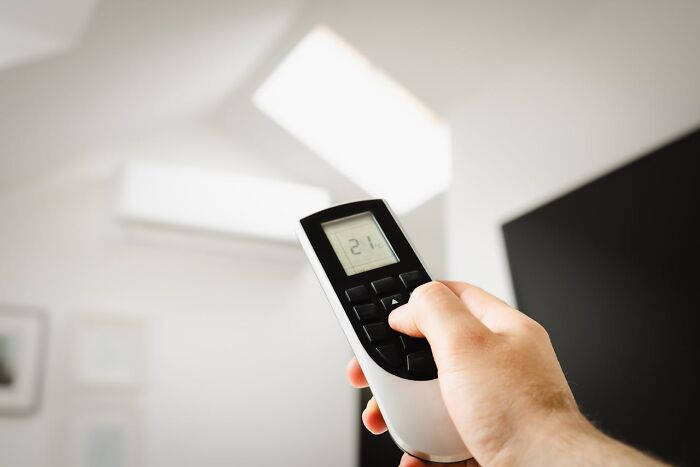 Hand holding a remote control pointing at a ceiling light, highlighting everyday things dangerous for health.