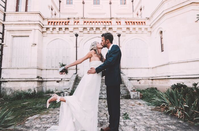 Bride and groom kissing outdoors in front of a historic building, illustrating unexpected moments in workplace scandals.
