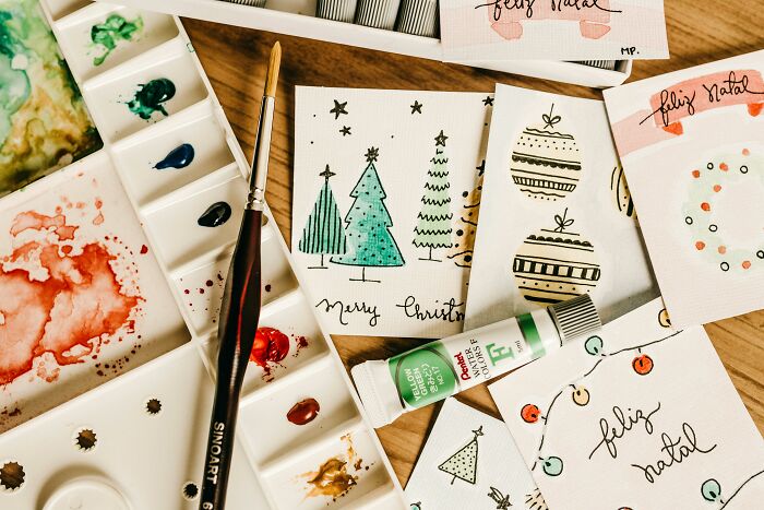 Watercolor paint set and handmade holiday cards featuring Christmas trees and ornaments, crafting ideas for holiday gifts.