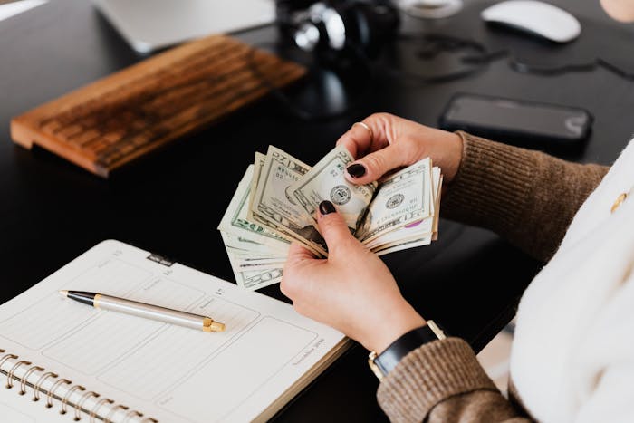 Woman counting cash at desk with planner and pen, illustrating grandparents combine birthday and Christmas gift scenario.