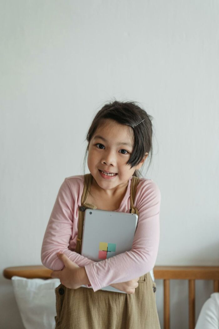 Young girl holding tablet indoors, representing modern parenting trends and technology use in families.