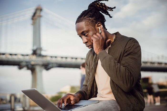 Young digital nomad working on laptop outdoors near a bridge, showcasing the unseen side of remote work life.