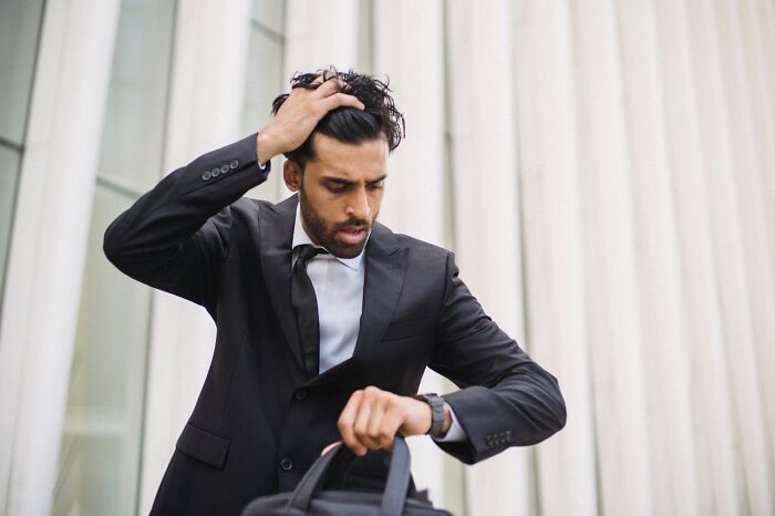 Man in a black suit checking watch with a confused expression, representing a glitch in the system moment.