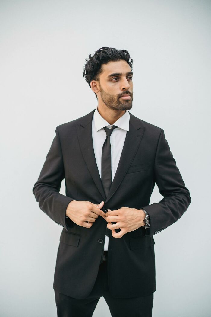 Man in a black suit adjusting jacket, embodying clever and sassy attitude in the heat of the moment.