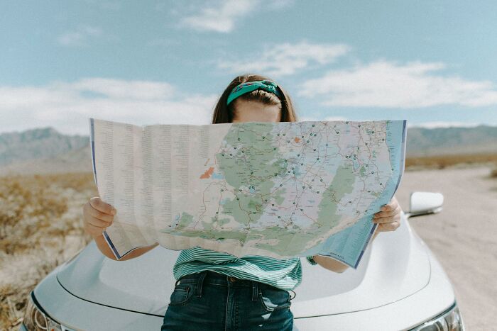 Person holding a map while leaning against a car in a desert landscape, testing geography knowledge and map mistakes. Person holding a map while leaning against a car in a desert landscape, testing geography knowledge and map mistakes.