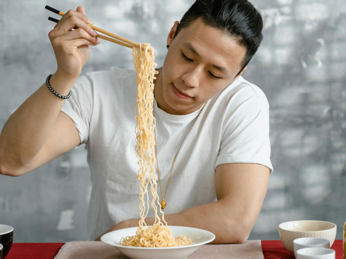 Young man enjoying noodles with chopsticks, highlighting picky eater demands affecting family Christmas menu choices.