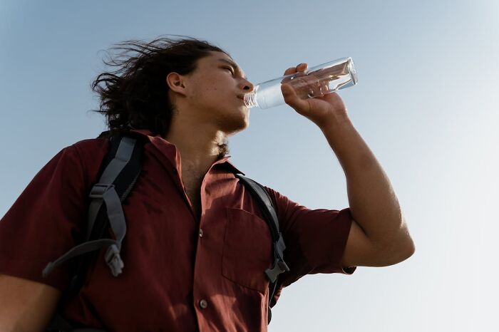 Young traveler with backpack drinking water under clear sky, reflecting crazy airport stories and travel adventures.