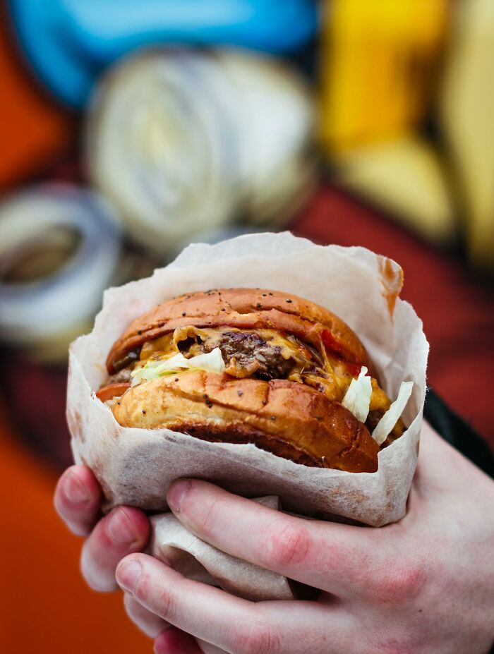 Close-up of a hand holding a cheeseburger wrapped in paper, illustrating a glitch in the system food hack.