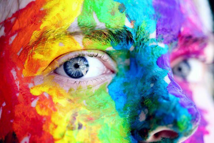 Close-up of a face covered in vibrant rainbow paint, highlighting the intense gaze and vivid colors for science facts.