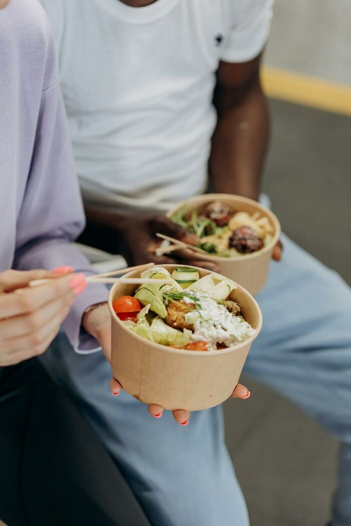 Two people holding bowls of fresh salad using chopsticks, showcasing a glitch in the system food hack.