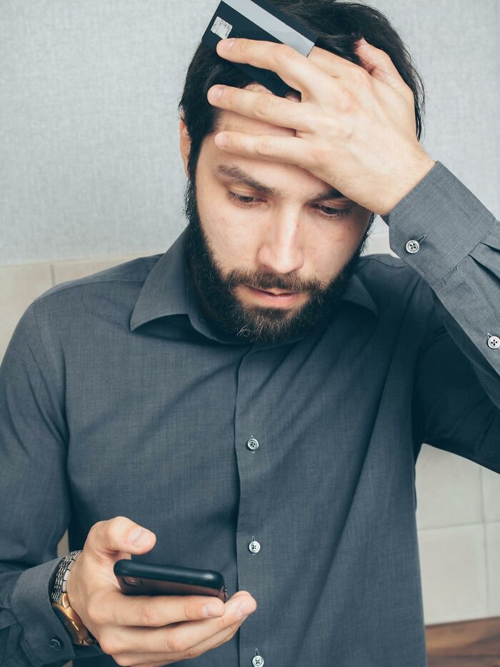Man with a beard holding a phone and credit card, looking worried about disturbing truths and horrifying information.