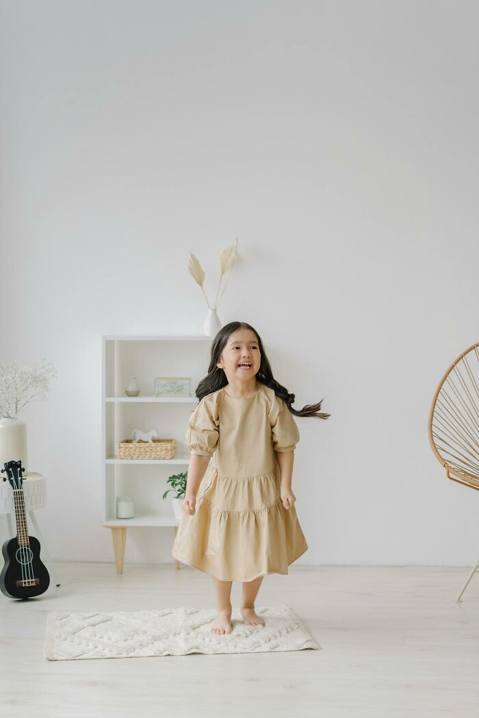 Young girl in a beige dress playing indoors in a modern parenting environment with minimalist decor and natural tones.
