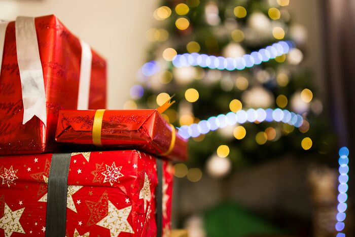 Stack of red wrapped presents in front of a decorated Christmas tree symbolizing horrible Christmas gifts.