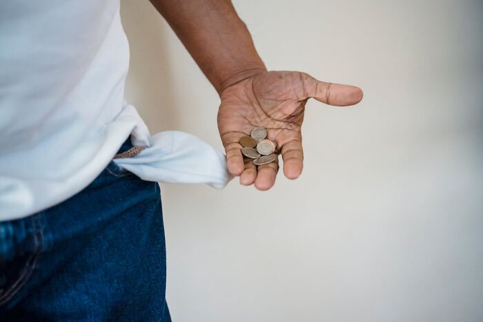 Person showing empty pocket and holding a few coins, illustrating a glitch in the system concept related to money.
