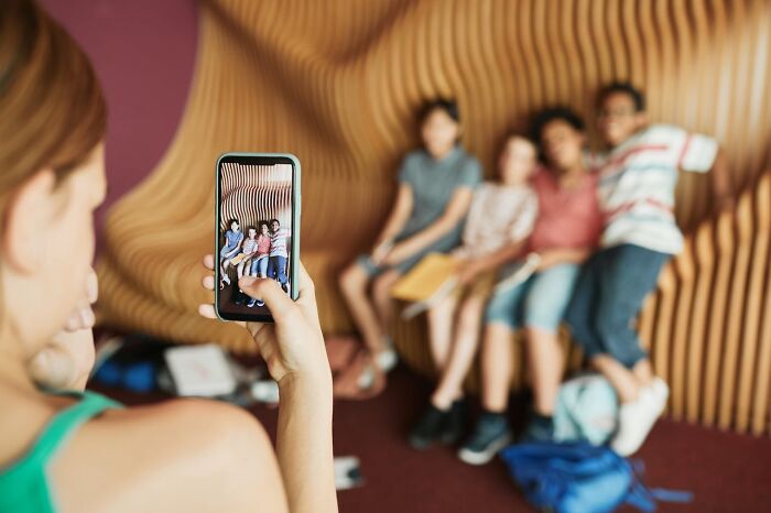 Person capturing a photo of children sitting on a wooden bench, illustrating modern parenting trends and family moments.