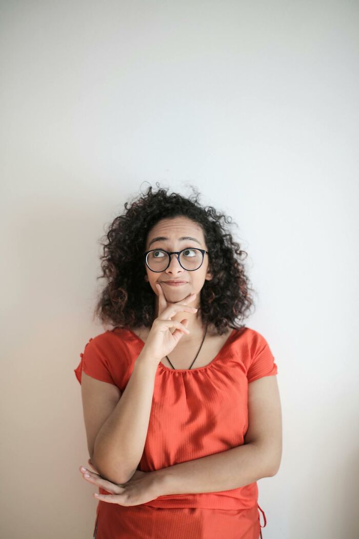 Young woman wearing glasses and red shirt, looking thoughtful and concerned about disturbing truths at night.