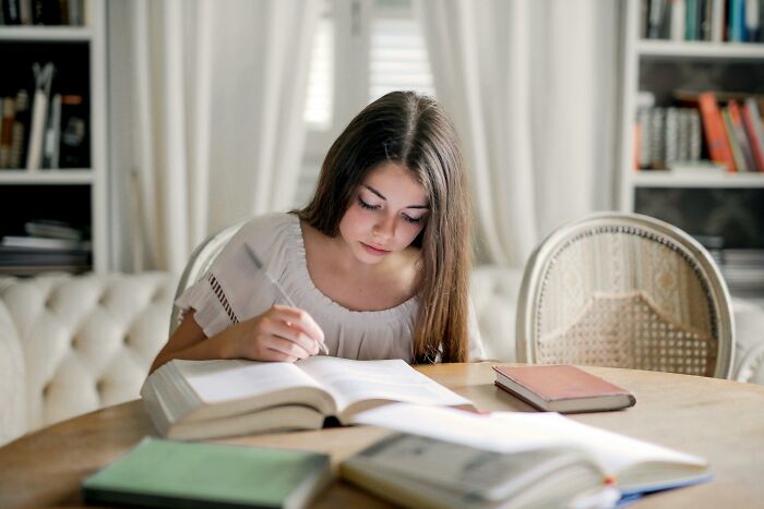 Young woman focused on solving an IQ quiz, sitting at a table with open books in a cozy study room. Young woman focused on solving an IQ quiz, sitting at a table with open books in a cozy study room.