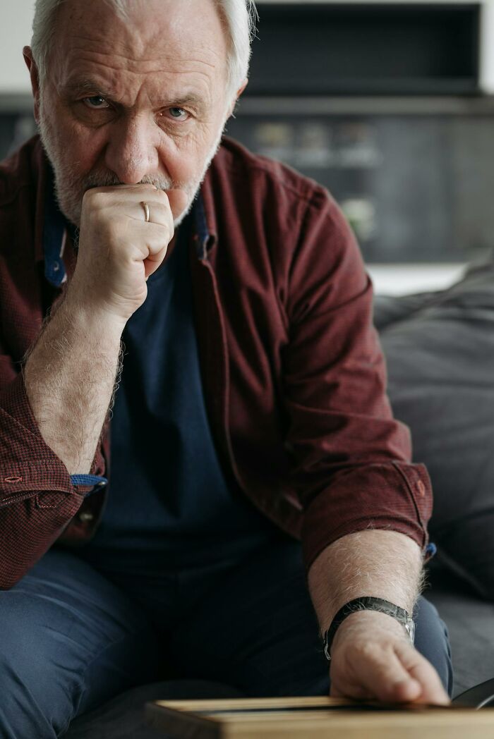 Elderly man looking disturbed and deep in thought, sitting on a couch reflecting on disturbing truths.