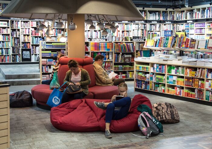People reading books in a cozy library surrounded by shelves filled with unusual personal belongings left at lost and found.