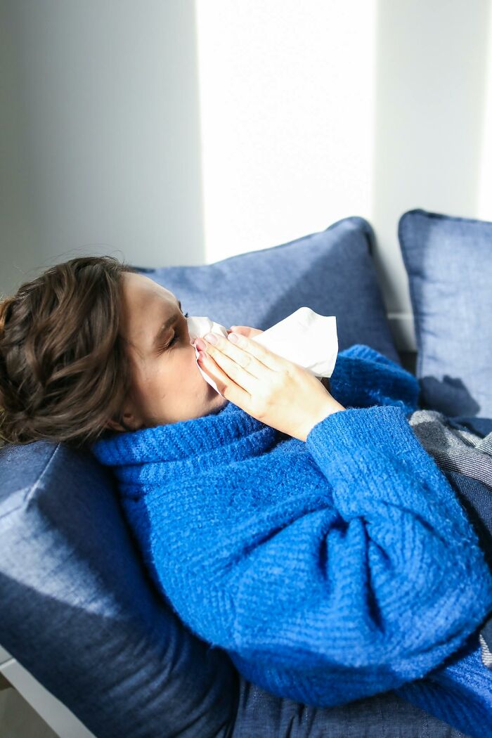 Woman in a blue sweater lying on a couch using a tissue, illustrating disturbing truths that keep you up at 2 AM.