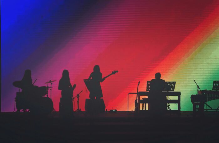 Silhouettes of a live band performing on stage with colorful gradient lights highlighting the music scene and band names.