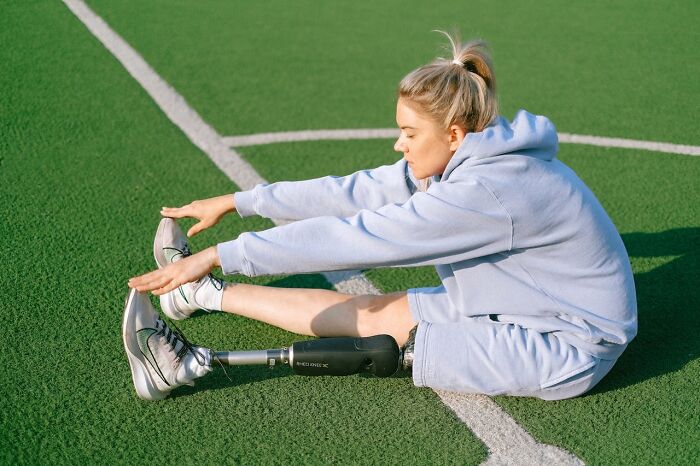 Young woman with prosthetic leg stretching on a sports field, showing unusual personal belongings at a lost and found.