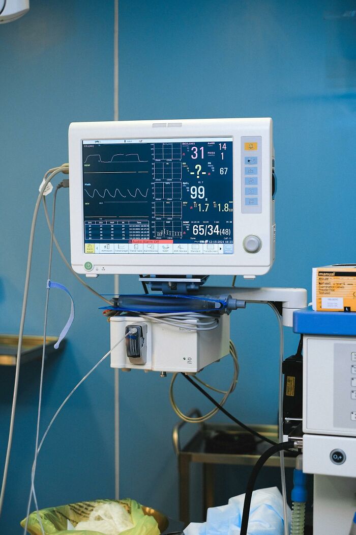 Medical monitor displaying vital signs and disturbing information in a hospital room with blue walls and equipment.