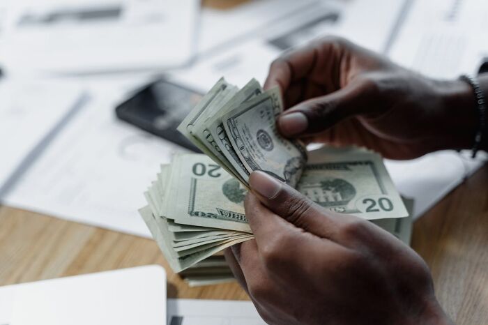 Hands counting US dollar bills on a desk with documents and a smartphone, illustrating disturbing truths about money.